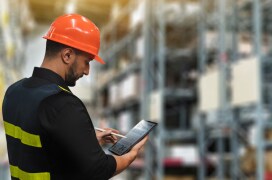 A worker reviews an inventory report on a tablet in a warehouse. A worker reviews an inventory report on a tablet in a warehouse.