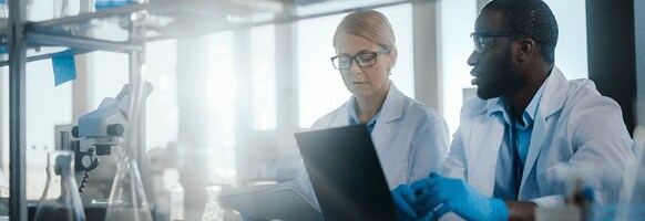 A woman and man discuss what they see on their computers in a chemistry lab. A woman and man discuss what they see on their computers in a chemistry lab.